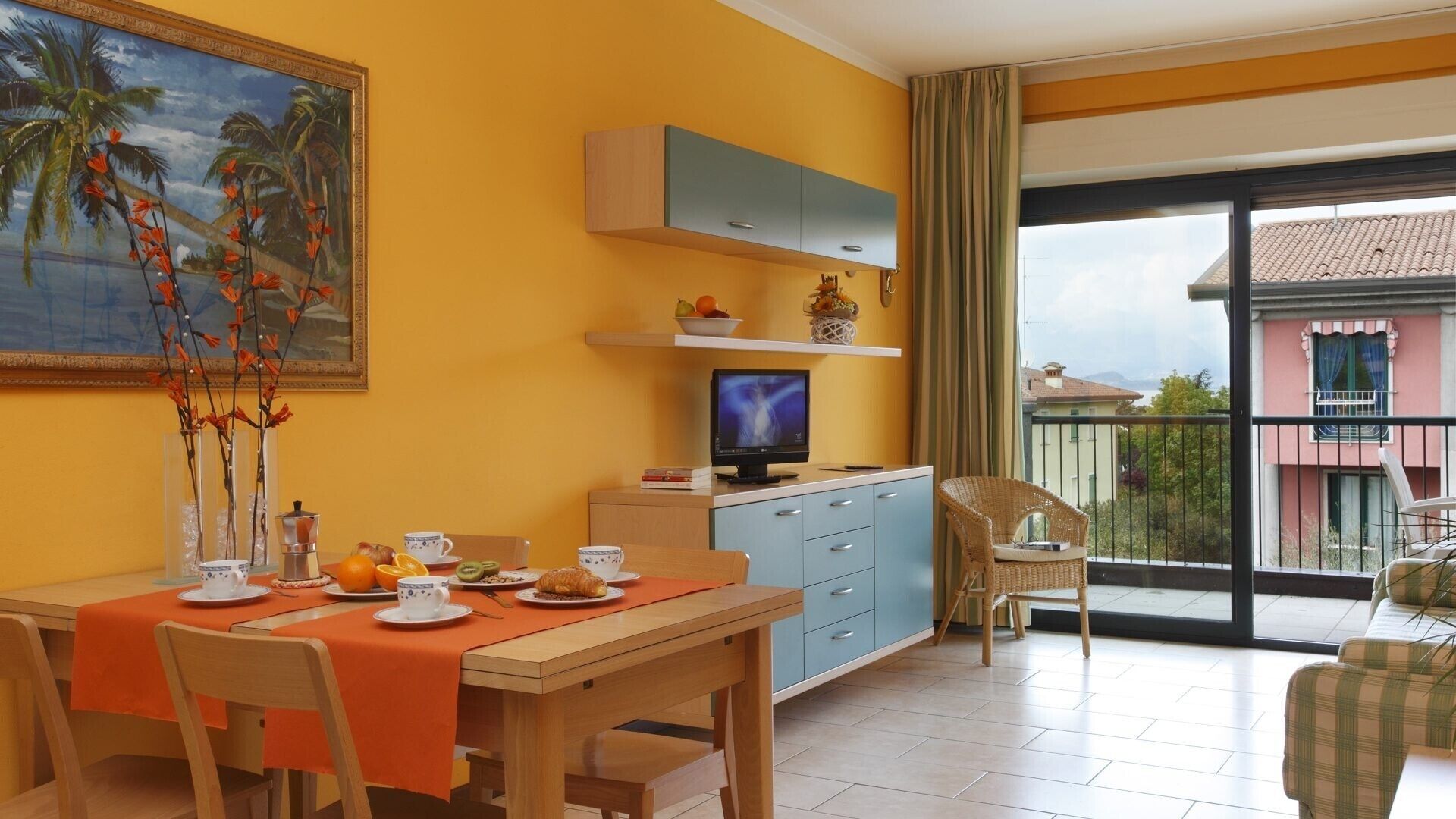 Un coin repas avec une table préparée pour le petit-déjeuner, un téléviseur et un balcon avec vue.