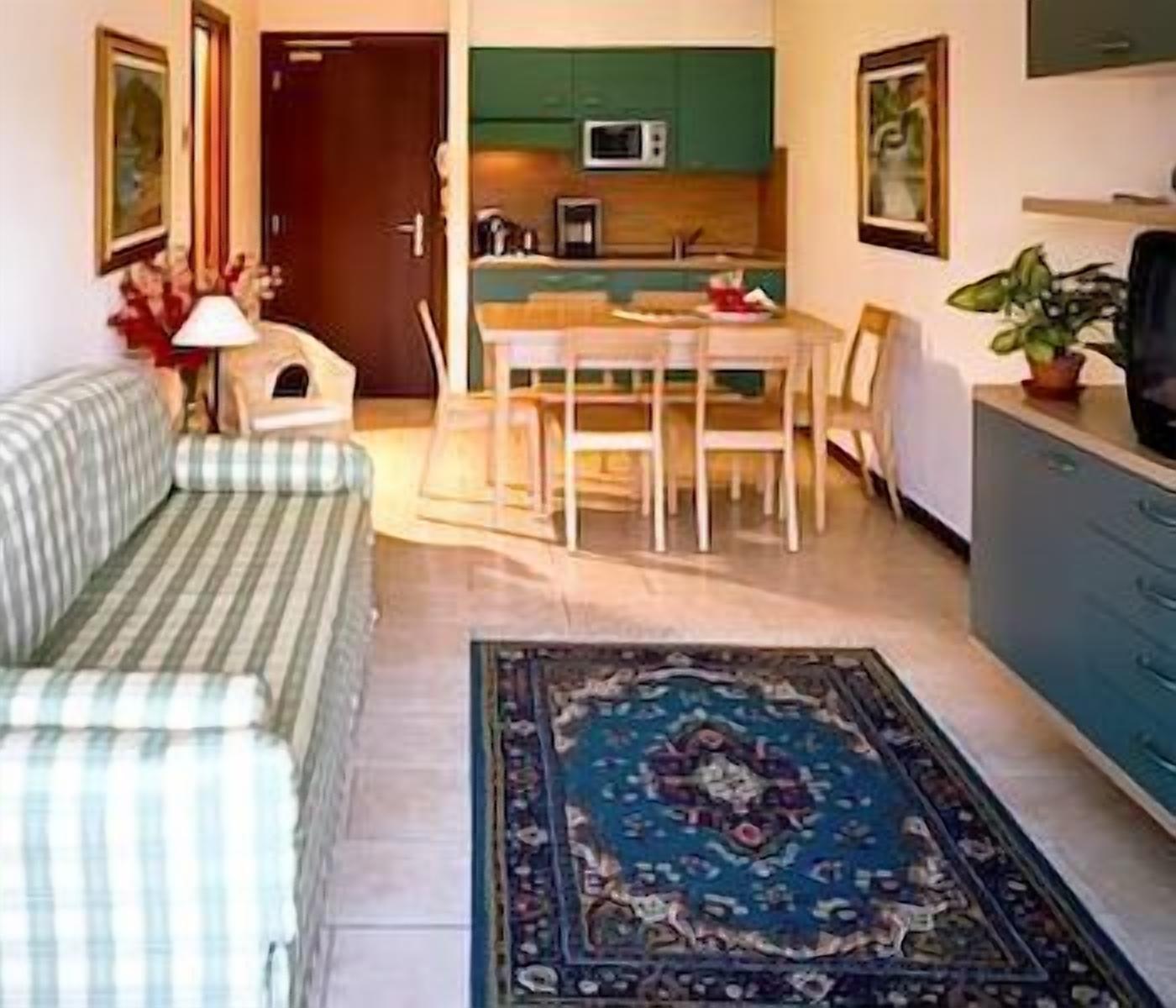 Un espace de vie compact comprenant un canapé à rayures, une table à manger avec des chaises, un coin cuisine avec un four à micro-ondes et un tapis bleu.
