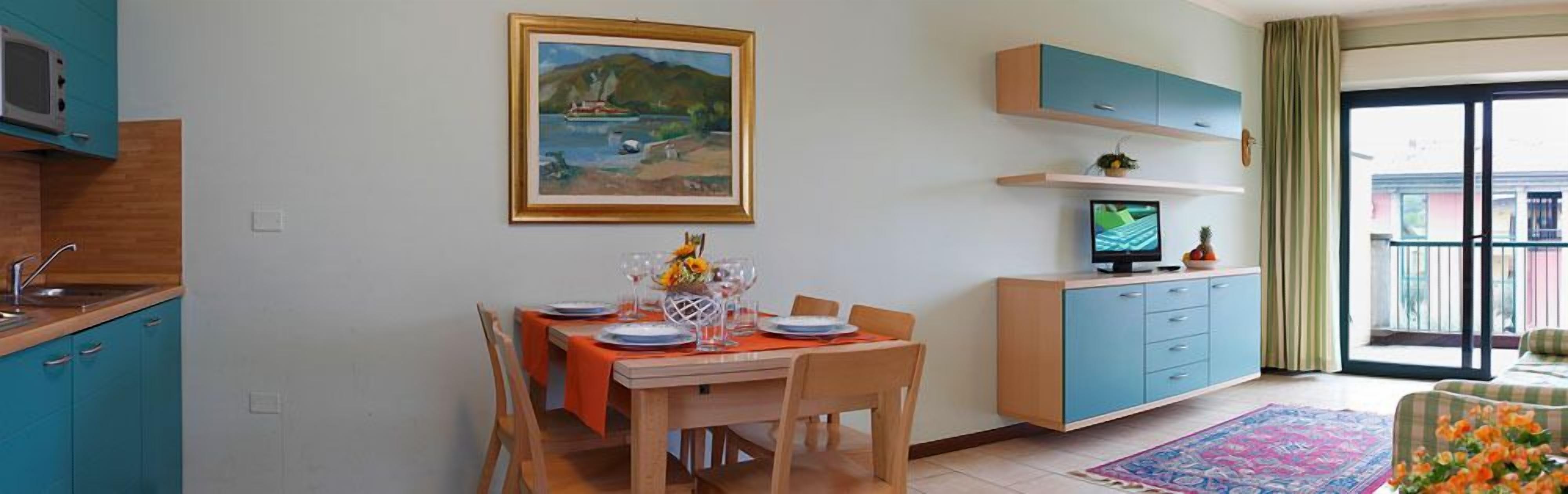 Een eethoek met een tafel voor vier personen, een schilderij erboven en een televisie op een standaard.