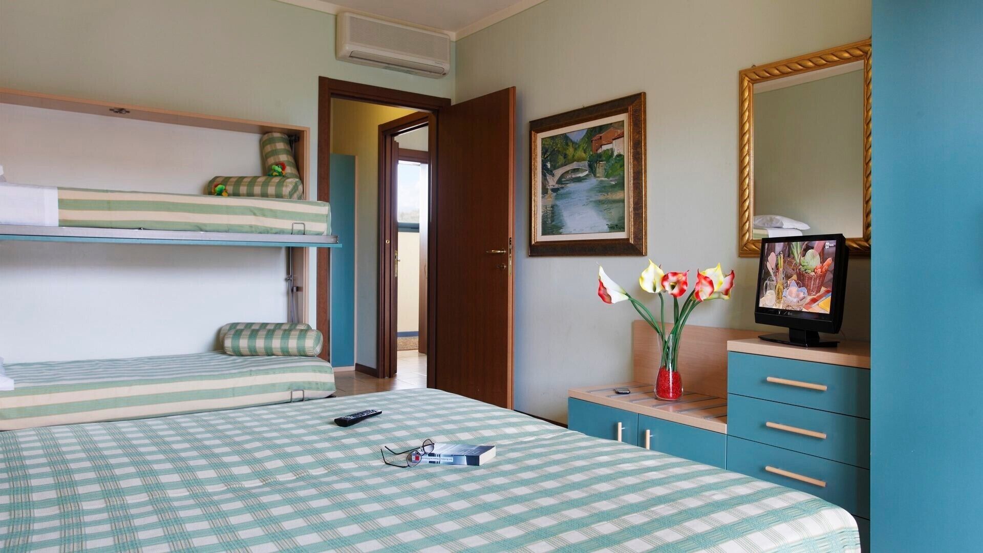 A room with bunk beds, a desk with a computer, a mirror, and a vase with flowers.