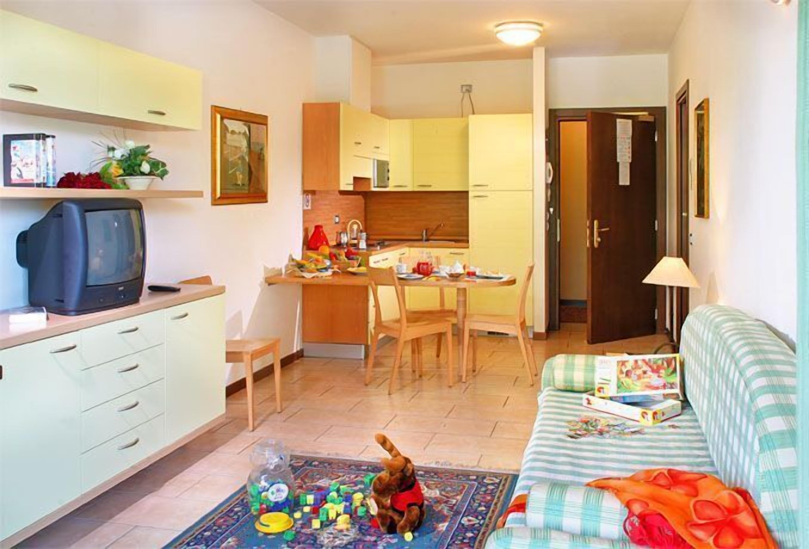 Un ambiente compatto con angolo cottura, zona pranzo e divano con tappetino giochi.