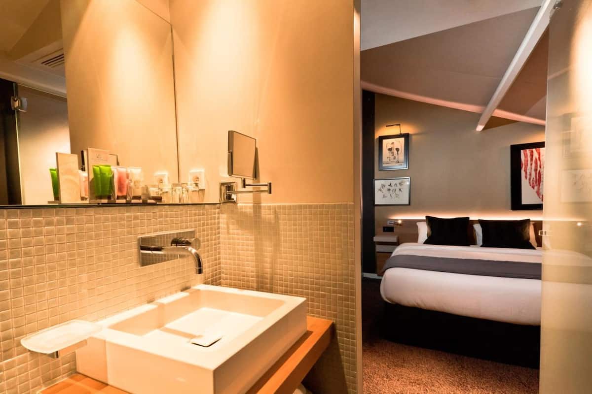 Un baño moderno con un lavabo grande y un espejo, una mesita de noche con un televisor, y una cama bien hecha.