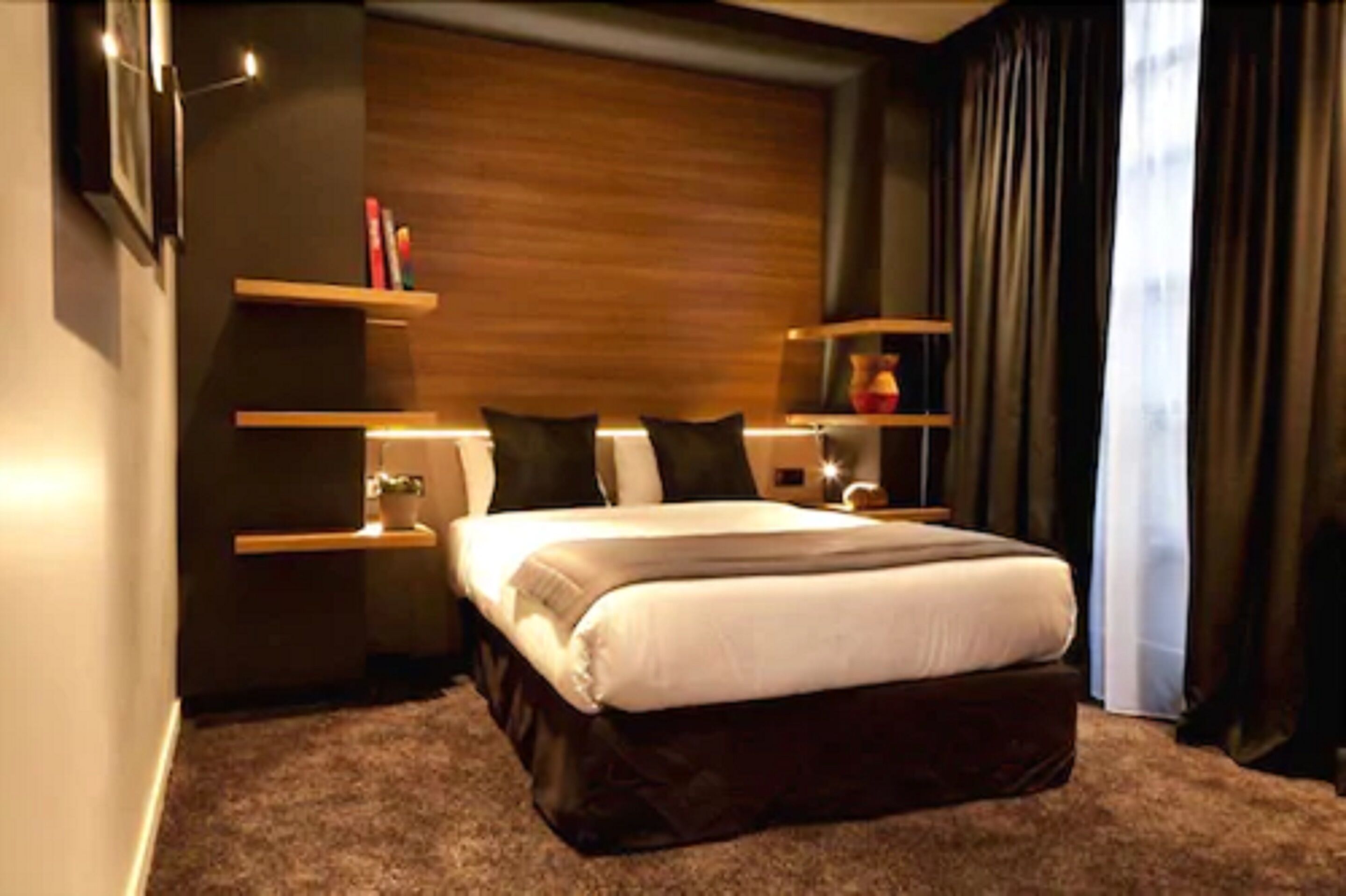 A modern bedroom with a large bed, dark curtains, and built-in shelves with decorative items.