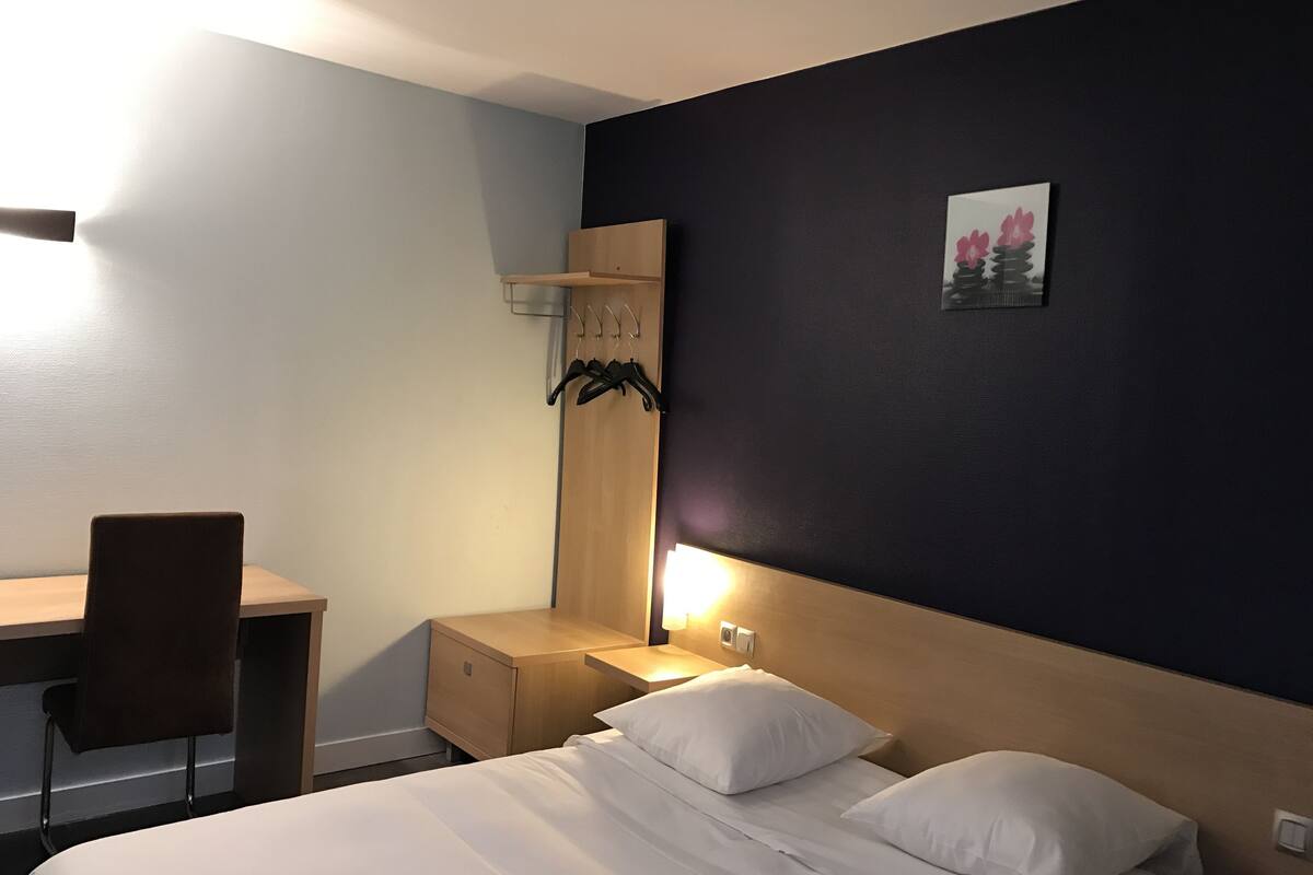 Ein Hotelzimmer mit einem Bett, einem Schreibtisch, einem Stuhl, einem Kleiderschrank und einem Nachttisch mit Lampe.