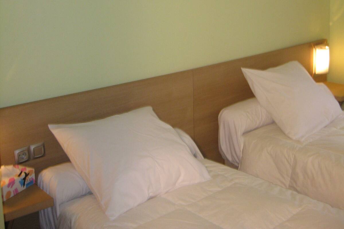Ein Hotelzimmer mit zwei Betten, einem Nachttisch, einer Wandlampe und einem Blumenbild in einem Rahmen.