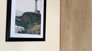 A framed photograph of a lighthouse on a cliff, a wooden panel wall, and a grey table.