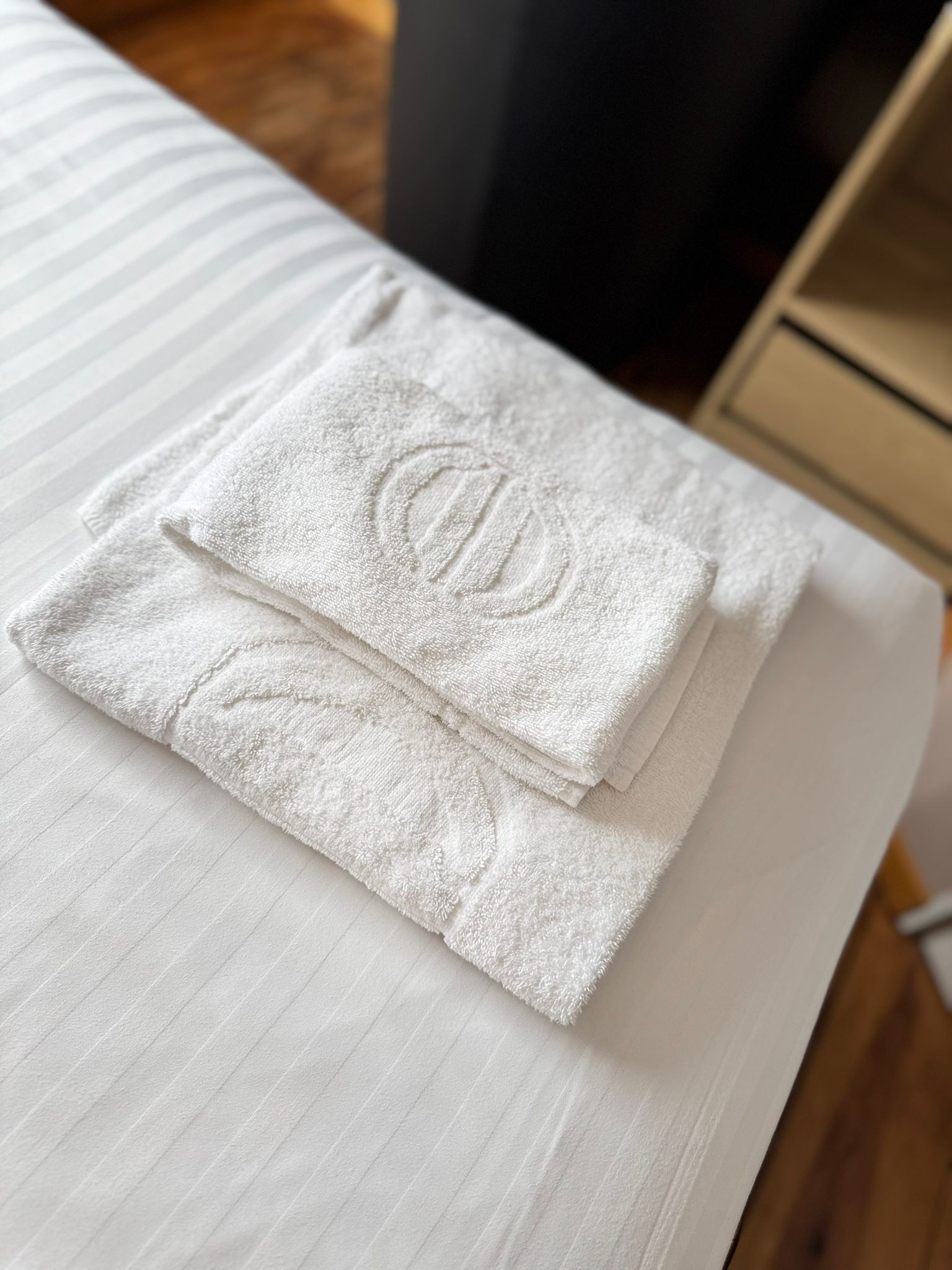 Une serviette blanche, soigneusement pliée, ornée d’un logo circulaire, posée sur une surface en bois.