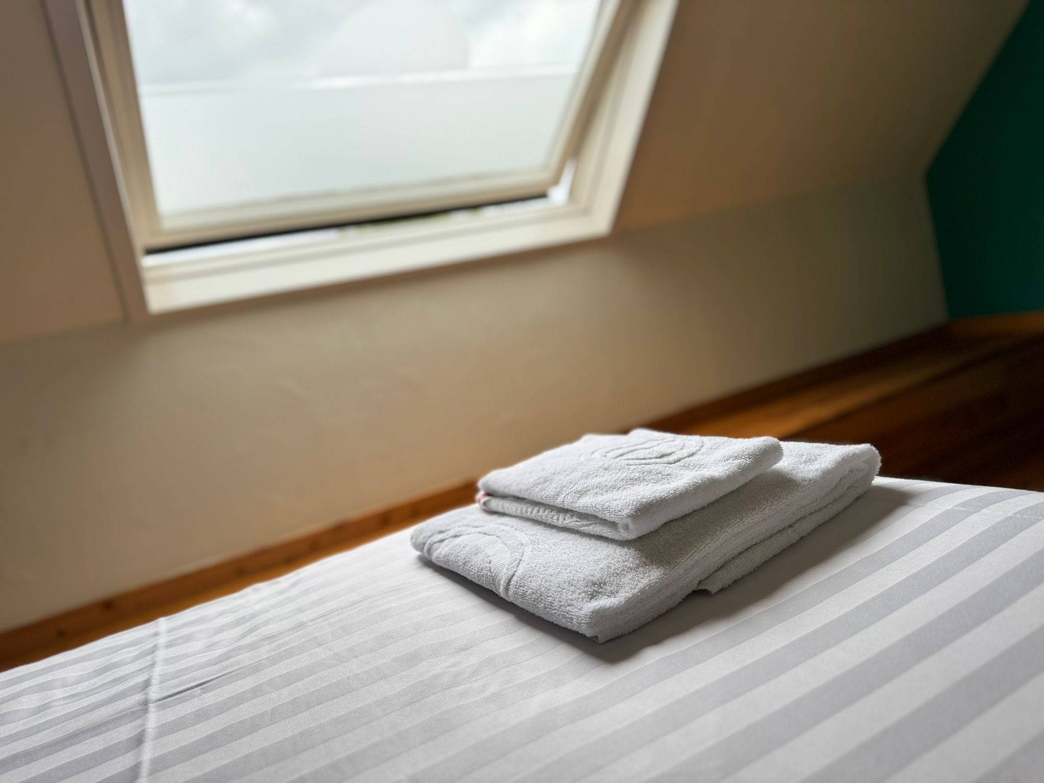 A neatly made bed with striped bedding and two folded towels on it.