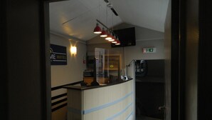 A hotel reception area with a counter, a sign reading "ME HOTEL", and a coffee machine.