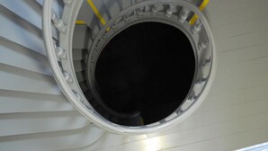 A circular window with a black center, surrounded by a white frame, set in a white wall with yellow safety lines.