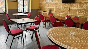 A dining area with red chairs and tables, a television mounted on the wall, and a window with a view of buildings.