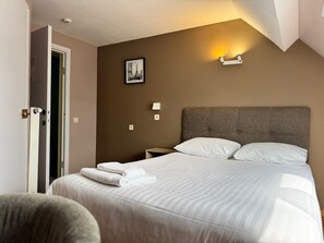 A hotel room with a bed, a nightstand, a wall-mounted lamp, and a door. - Family Hotel (Wavre)