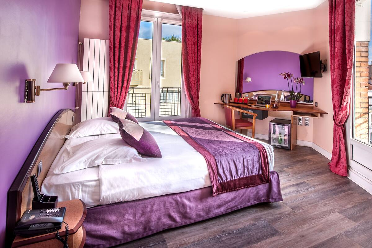 A bedroom with a bed, a desk, a chair, a TV, and a balcony.