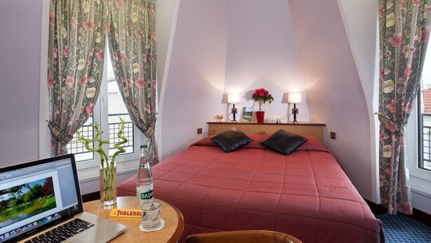 A hotel room with a bed, a desk with a laptop, a bottle of water, and a vase with a plant. - Hotel Virgina (Paris)