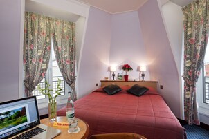 Habitación de hotel con una cama, un escritorio con una computadora portátil, una botella de agua y un florero con una planta.