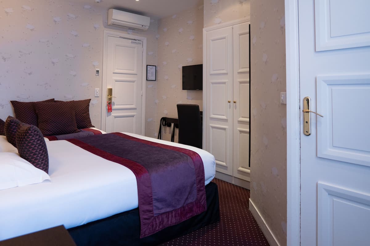 A hotel room with a bed, a desk, a chair, a TV, and a wardrobe.