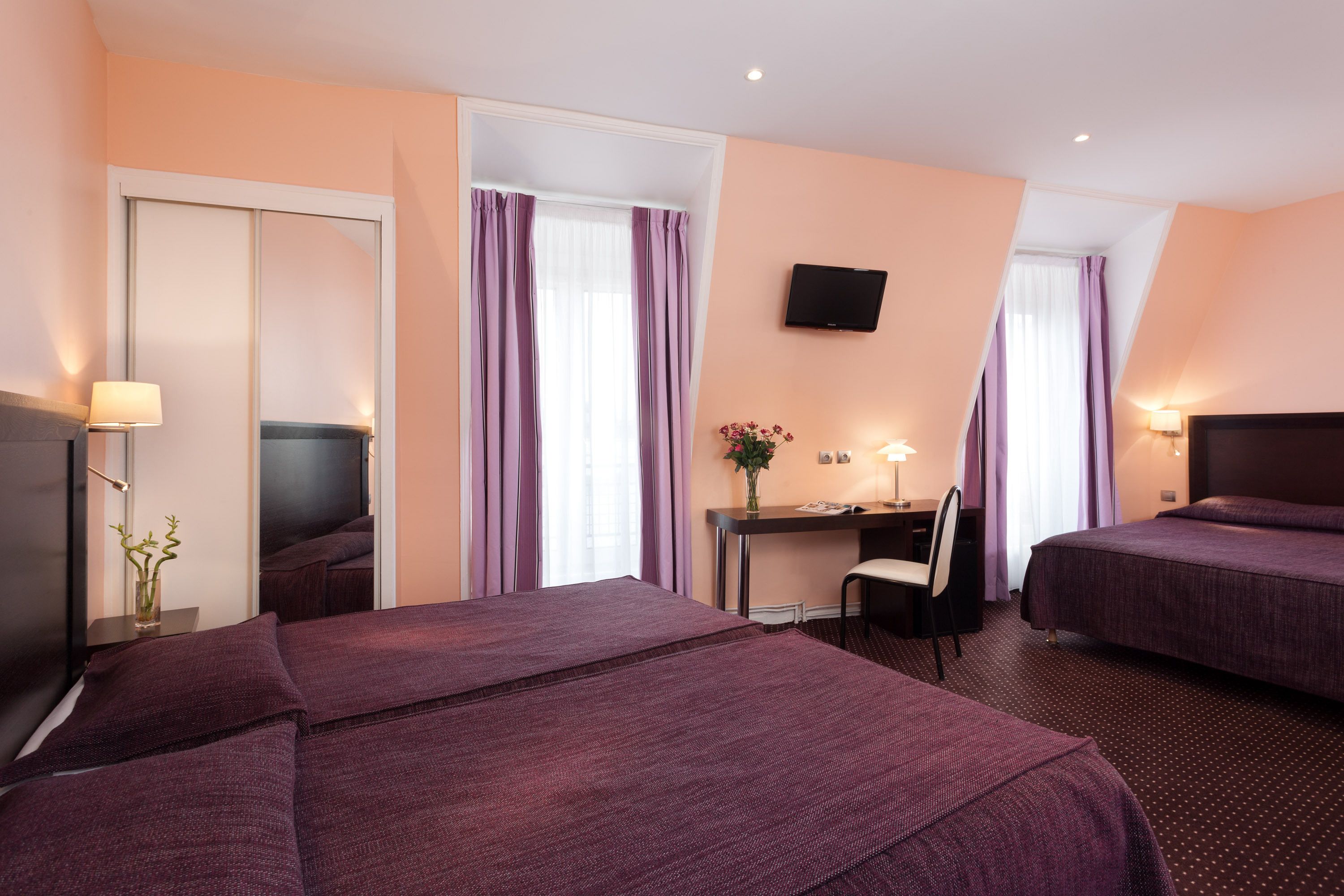 A hotel room with two beds, a desk, a chair, a TV, and a mirror.