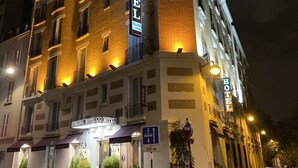 A multi-story hotel with illuminated signage, a ground-level entrance, and a visible parking sign indicating a 30m drop-off zone. - Hotel Virgina (Paris)