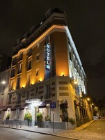 Un hotel de varios pisos con señalización iluminada, entrada a nivel de suelo y un letrero de estacionamiento que indica una zona de acceso de 30 metros.