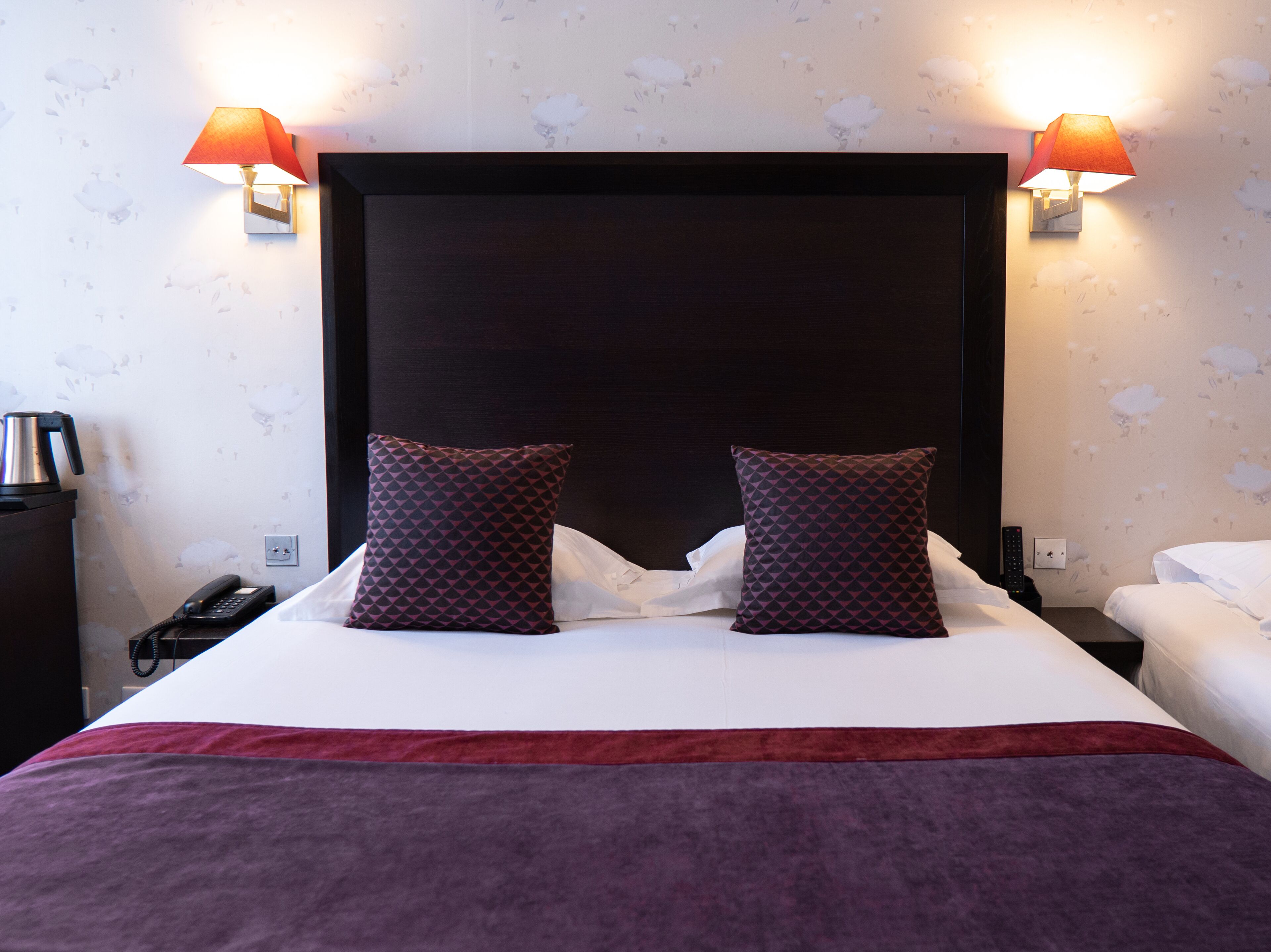 Une chambre d’hôtel avec un grand lit, deux oreillers, une table de chevet avec un téléphone et deux lampes fixées au mur.
