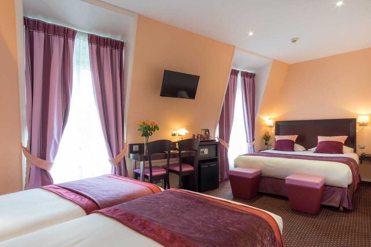 A hotel room with two beds, a desk, a TV, and a small seating area.