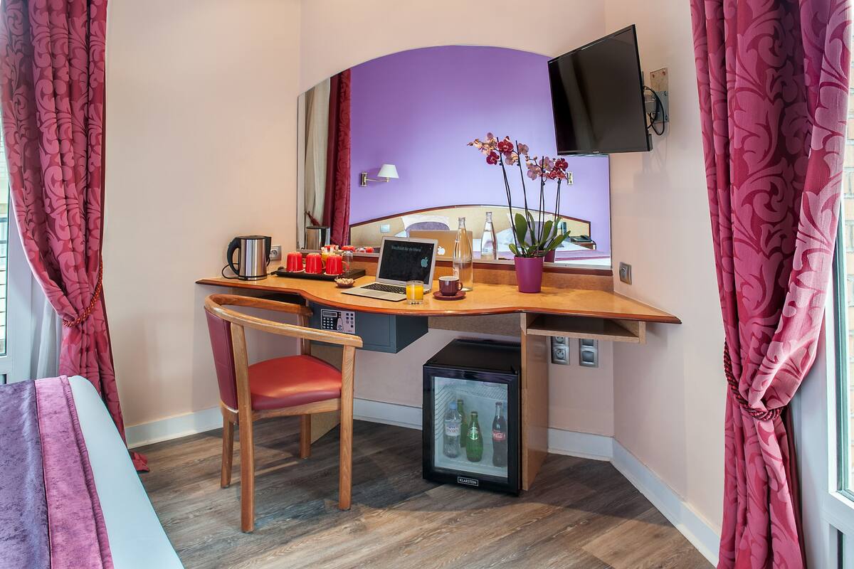 A compact hotel room with a desk, chair, and a small refrigerator.