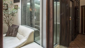 Un intérieur moderne avec un ascenseur en verre, un canapé beige et une plante en pot.