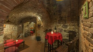 Un intérieur aux murs de pierre, avec des tables et des chaises, un luminaire suspendu et une croix accrochée au mur.