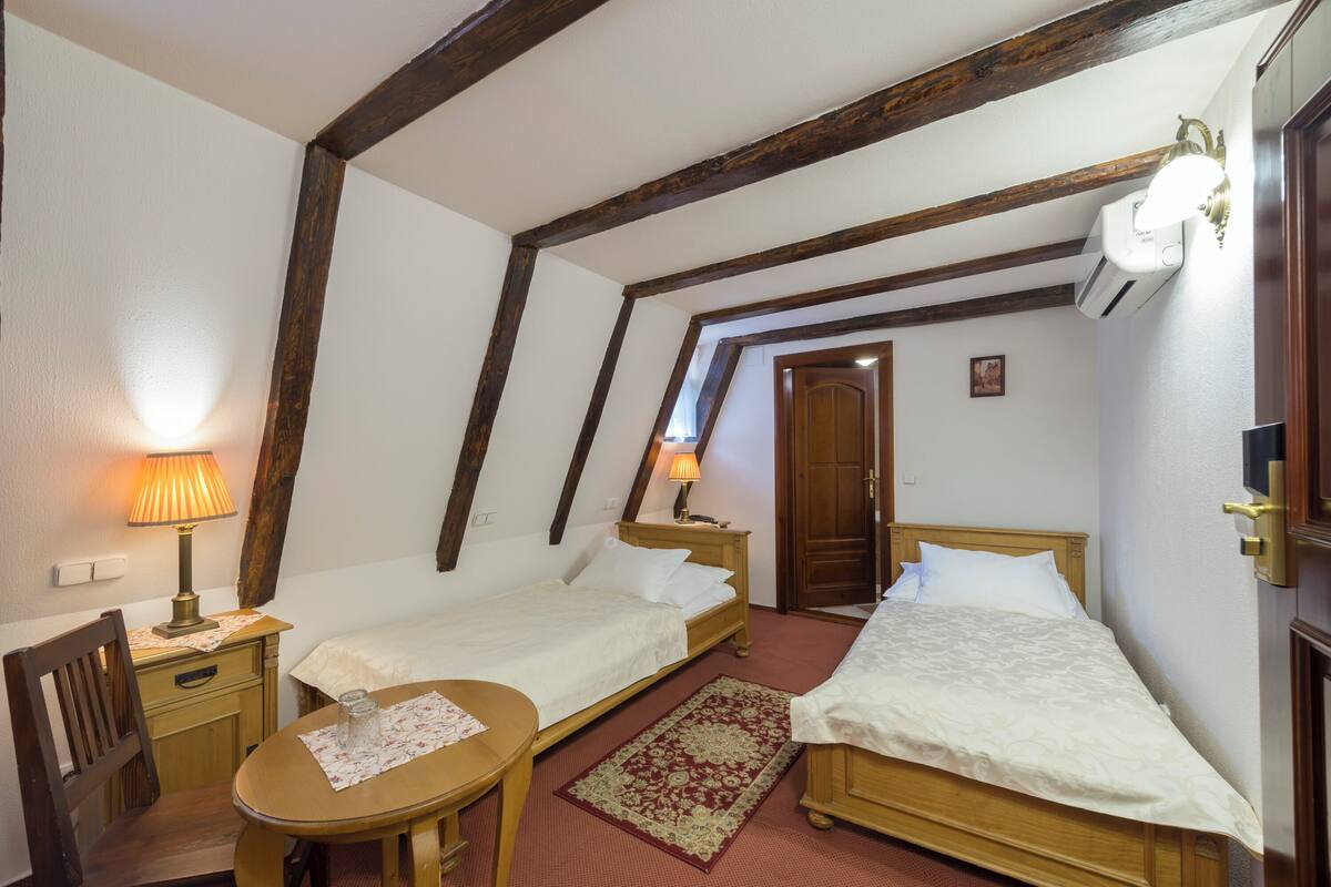 Ein Zimmer mit zwei Einzelbetten, einem Holztisch mit Stuhl, einer Lampe und einem roten Teppich.