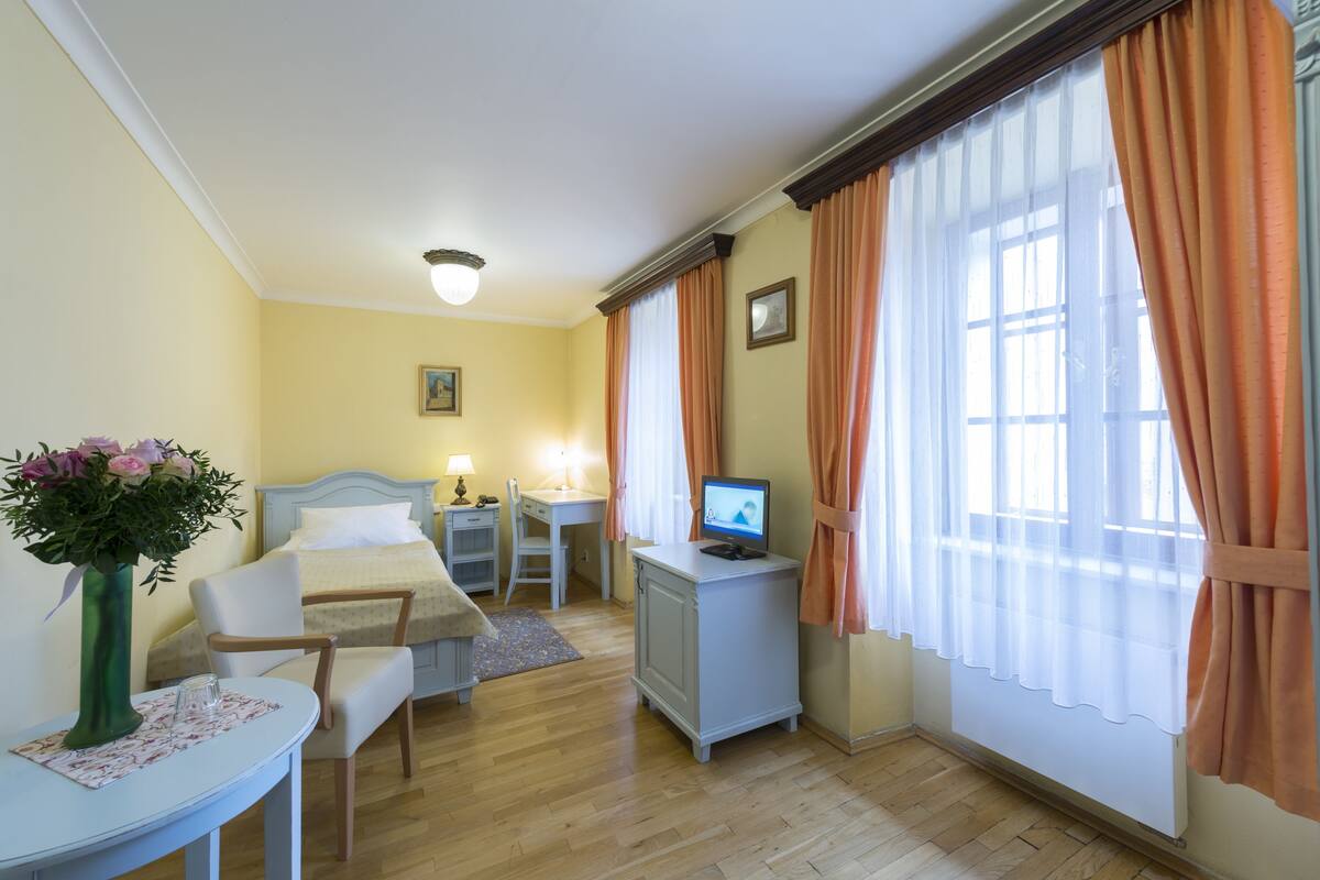 Ein Hotelzimmer mit Bett, Schreibtisch, Stuhl, Fernseher und einem Vorhangfenster.