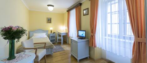 A hotel room with a bed, desk, chair, TV, and a window with curtains.