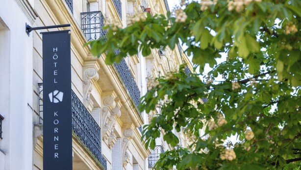 Letrero de hotel con el nombre "HOTEL KORNER" y fachada de edificio con balcones y molduras decorativas.