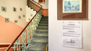 Una escalera con barandillas de metal decorativas, un grabado histórico enmarcado y un letrero de salida de emergencia.