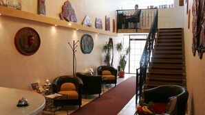 A hotel lobby with a reception desk, seating area, staircase, and artwork on the walls. - Manzard Panzio (Budapest)