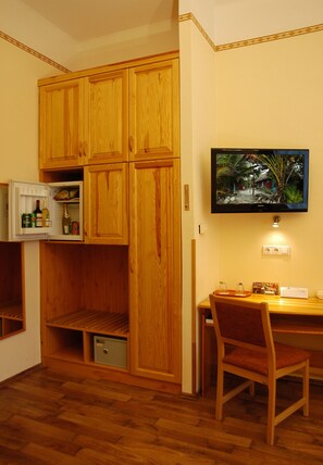 A compact kitchen with wooden cabinets, a refrigerator, and a dining area with a chair and table. - Manzard Panzio (Budapest)