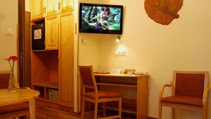 A cozy room with wooden furniture, a TV on the wall, and a small desk with a chair. - Manzard Panzio (Budapest)