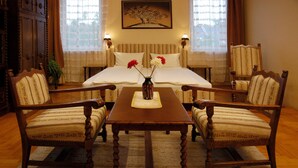 A hotel room with a large bed, two armchairs, a wooden table, and a vase with flowers. - Manzard Panzio (Budapest)
