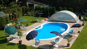 A swimming pool with lounge chairs and umbrellas, surrounded by a well-maintained lawn and a greenhouse structure. - Manzard Panzio (Budapest)