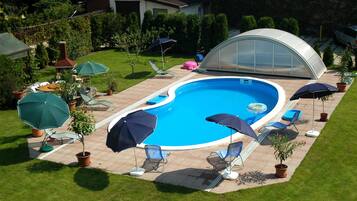 Una piscina con sillas de descanso y sombrillas, rodeada por un césped cuidado y una estructura tipo invernadero.