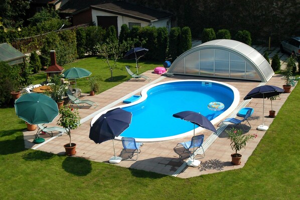 A swimming pool with lounge chairs and umbrellas, surrounded by a well-maintained lawn and a greenhouse structure.
