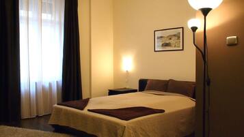A hotel room with a bed, a nightstand, a lamp, a picture on the wall, and a window with curtains.