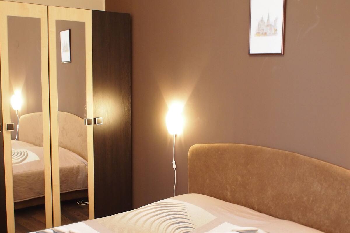 A hotel room with a bed, a wardrobe, a bedside lamp, and a framed picture on the wall.