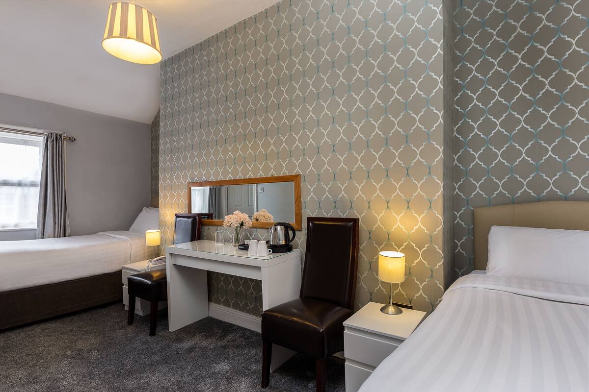 Ein Hotelzimmer mit Bett, Schreibtisch mit Stuhl, einem kleinen Tisch mit Lampe und einem Spiegel.
