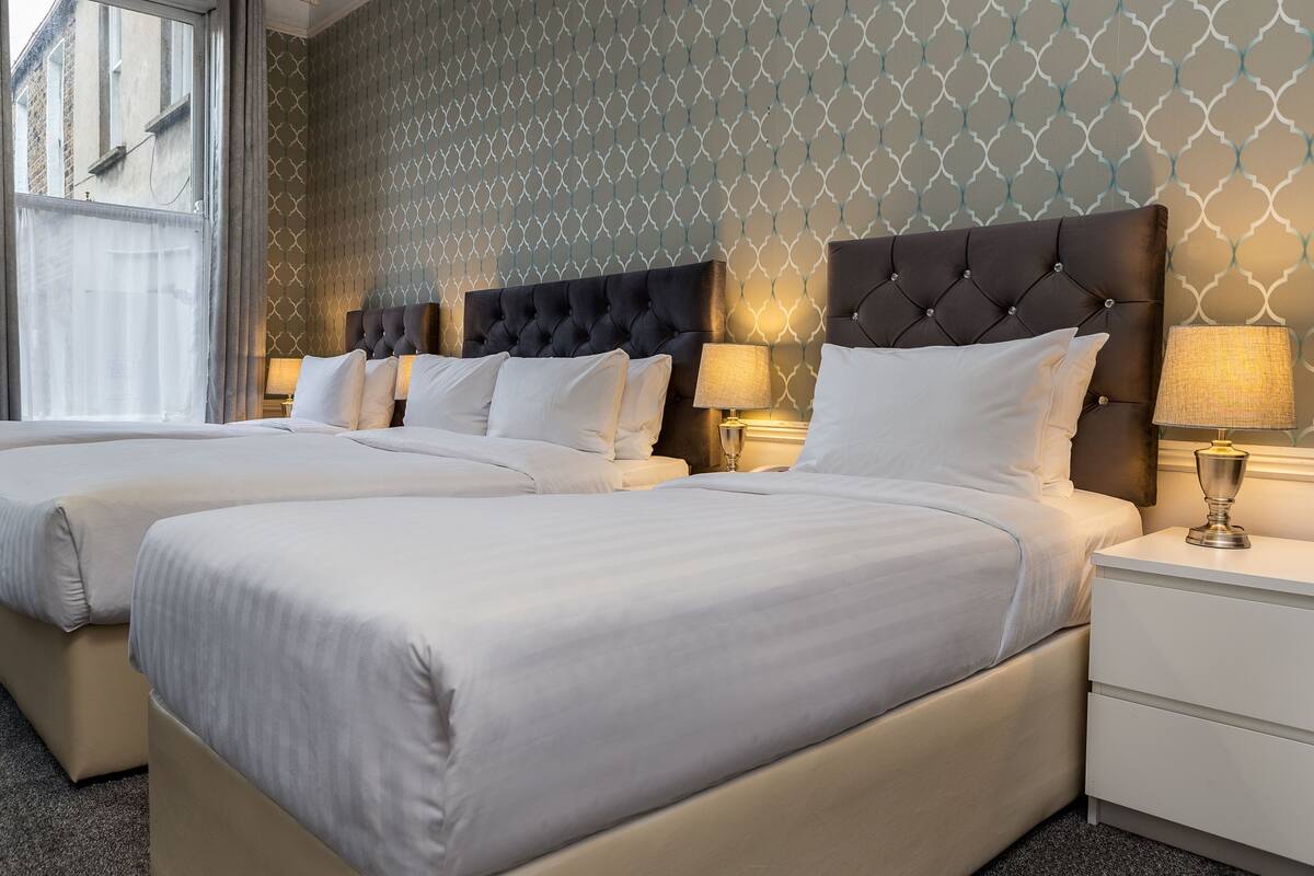 Ein Hotelzimmer mit zwei Betten, einer Wand mit Muster und einem Fenster mit Vorhängen.