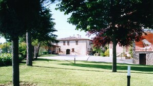 A grassy courtyard with a stone building, trees, and a clear sky. - Agriturismo Il Borghetto (Montefalco)