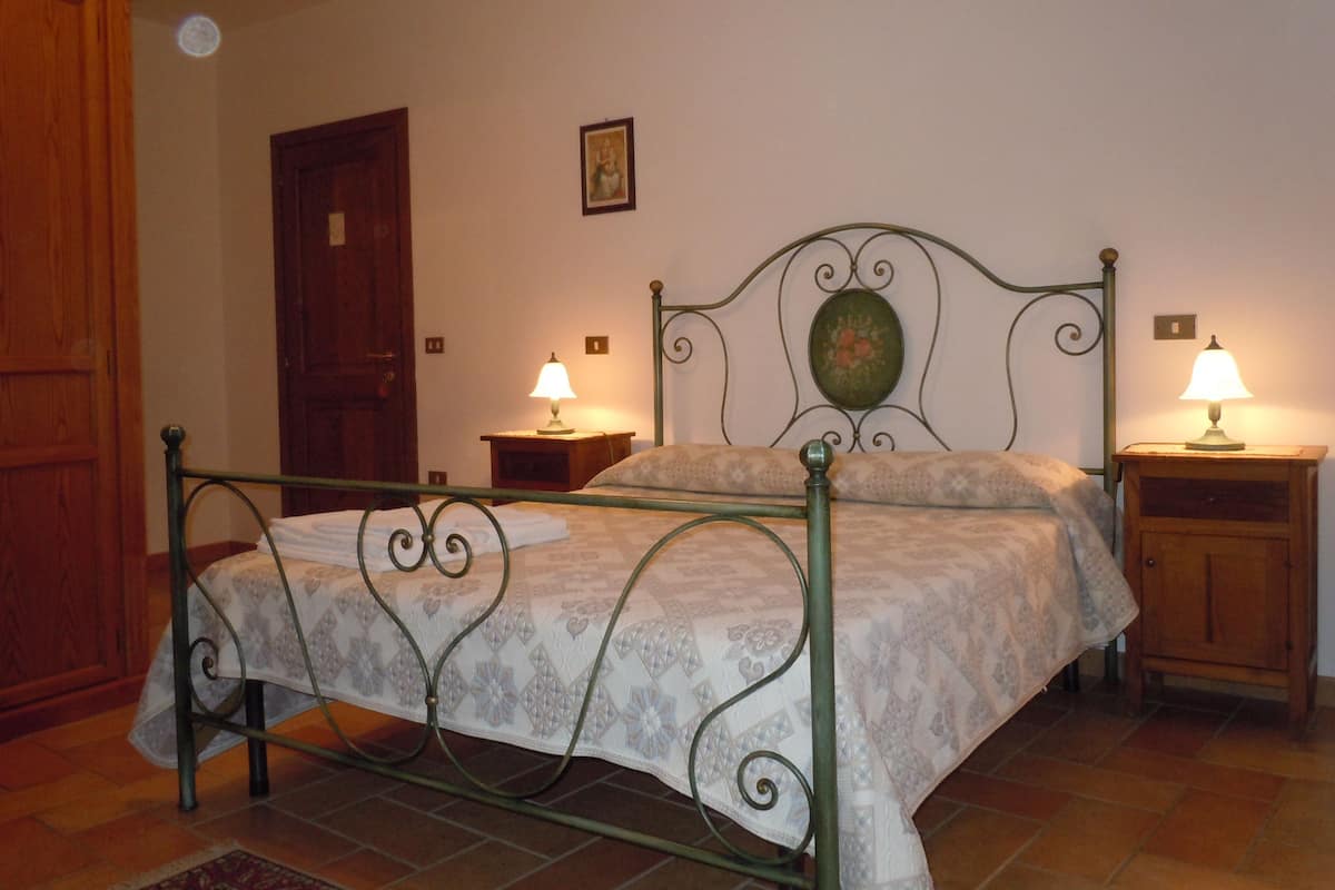 Ein Schlafzimmer mit Metallbettgestell, zwei Nachttischen mit Lampen, einer Holztür und einem an der Wand montierten Lichtschalter.