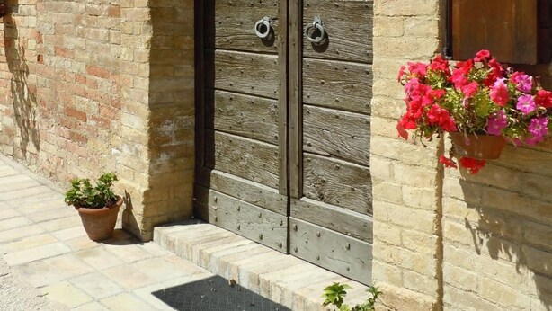 A stone building with a wooden door and a window with a shutter. There are potted plants on the ground. - Agriturismo Il Borghetto (Montefalco)