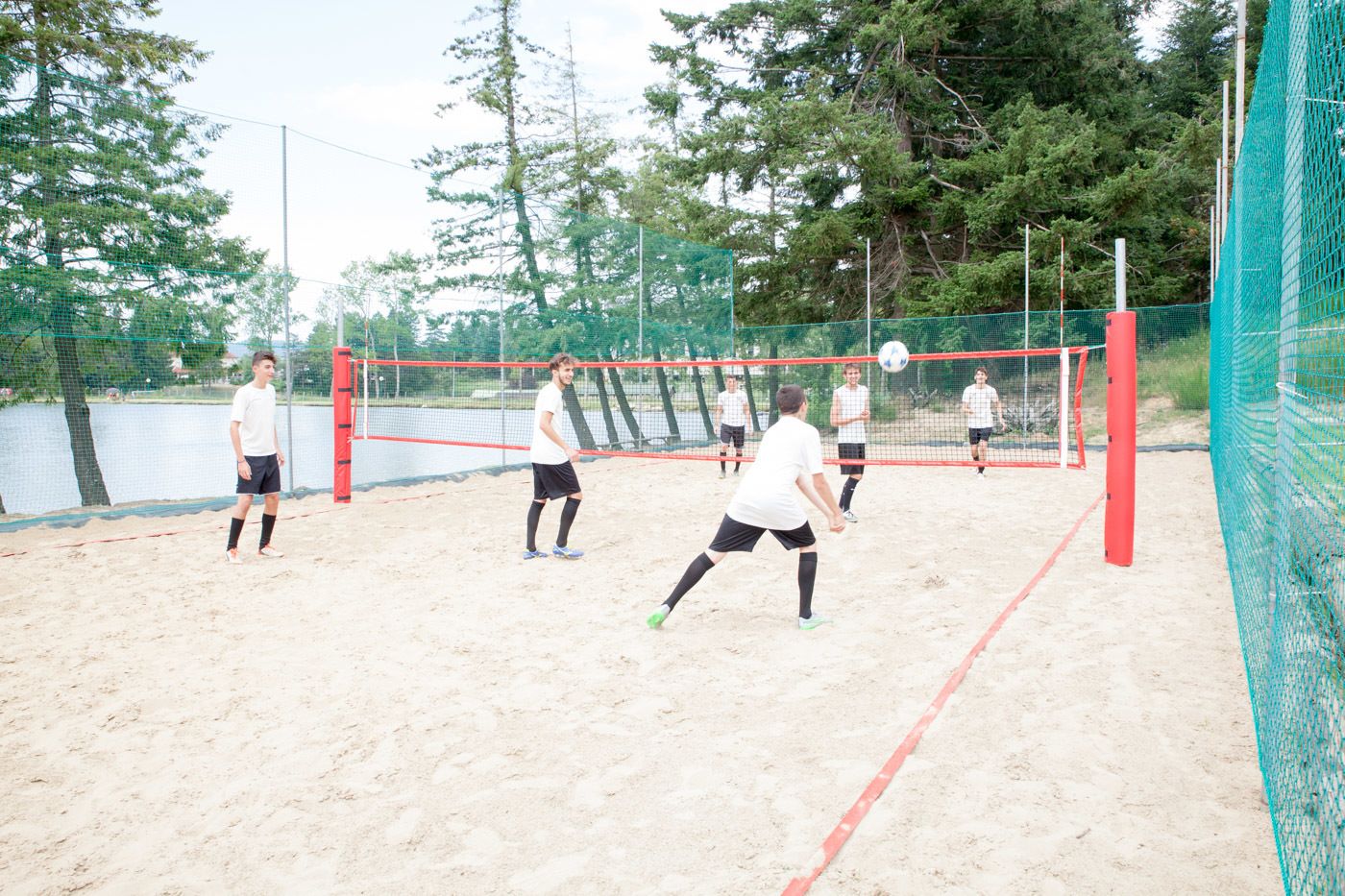 Una spiaggia con una rete da pallavolo, giocatori in bianco e nero e alberi intorno.