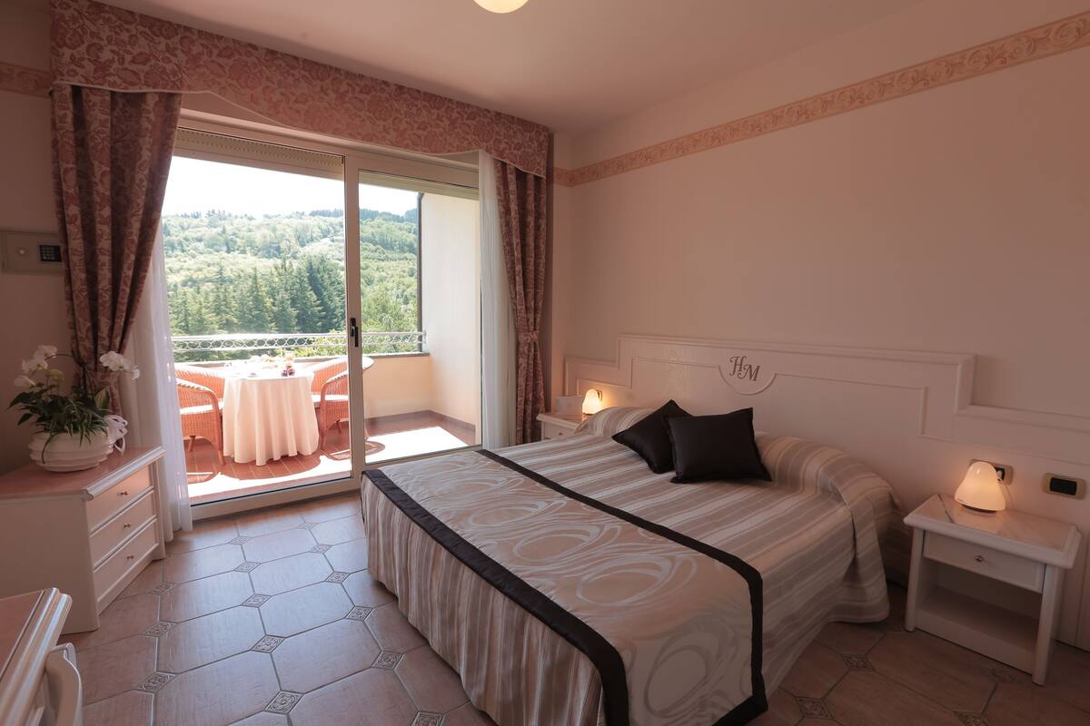 Una camera da letto con un letto grande, un comodino, una cassettiera e vista su un balcone con mobili da esterno.
