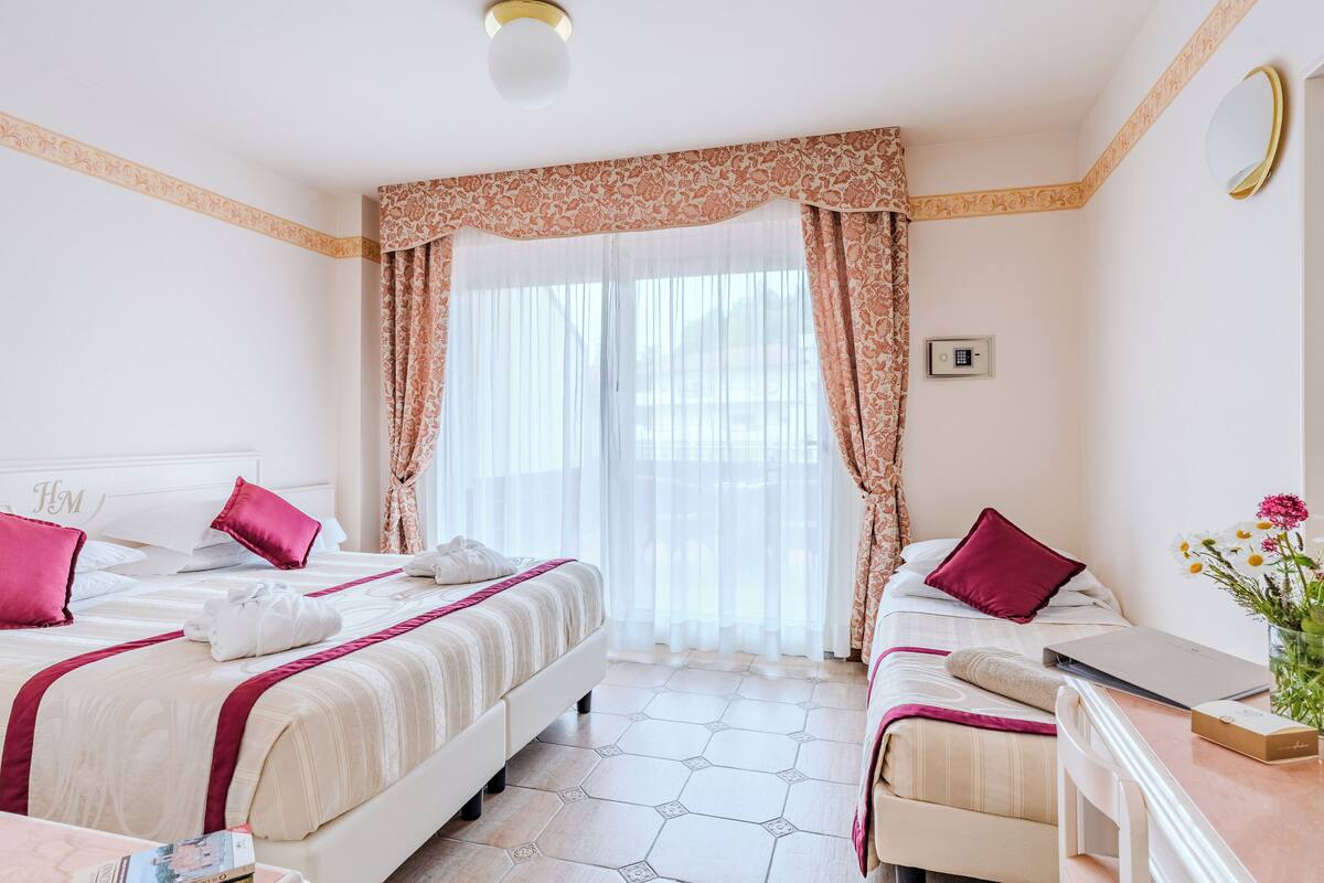 Una camera d'albergo con due letti, una scrivania e una finestra con tende.